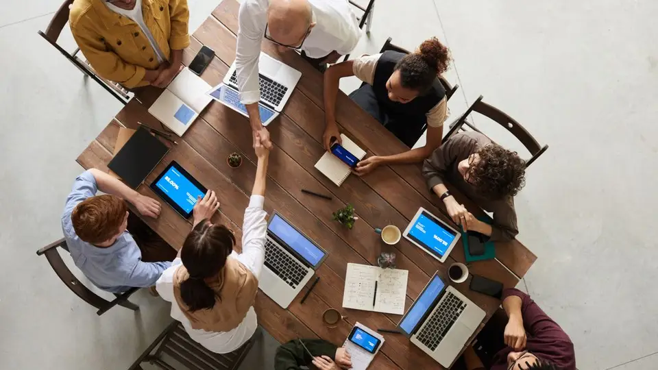 An overhead view of a team collaborating around laptops and tablets at a wooden table