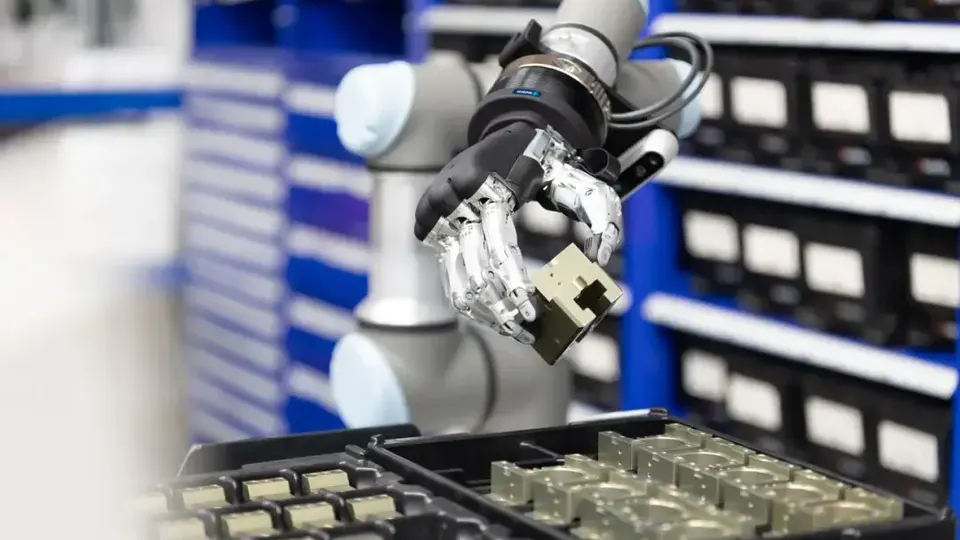 A robotic hand gripping an industrial component in front of warehouse bins