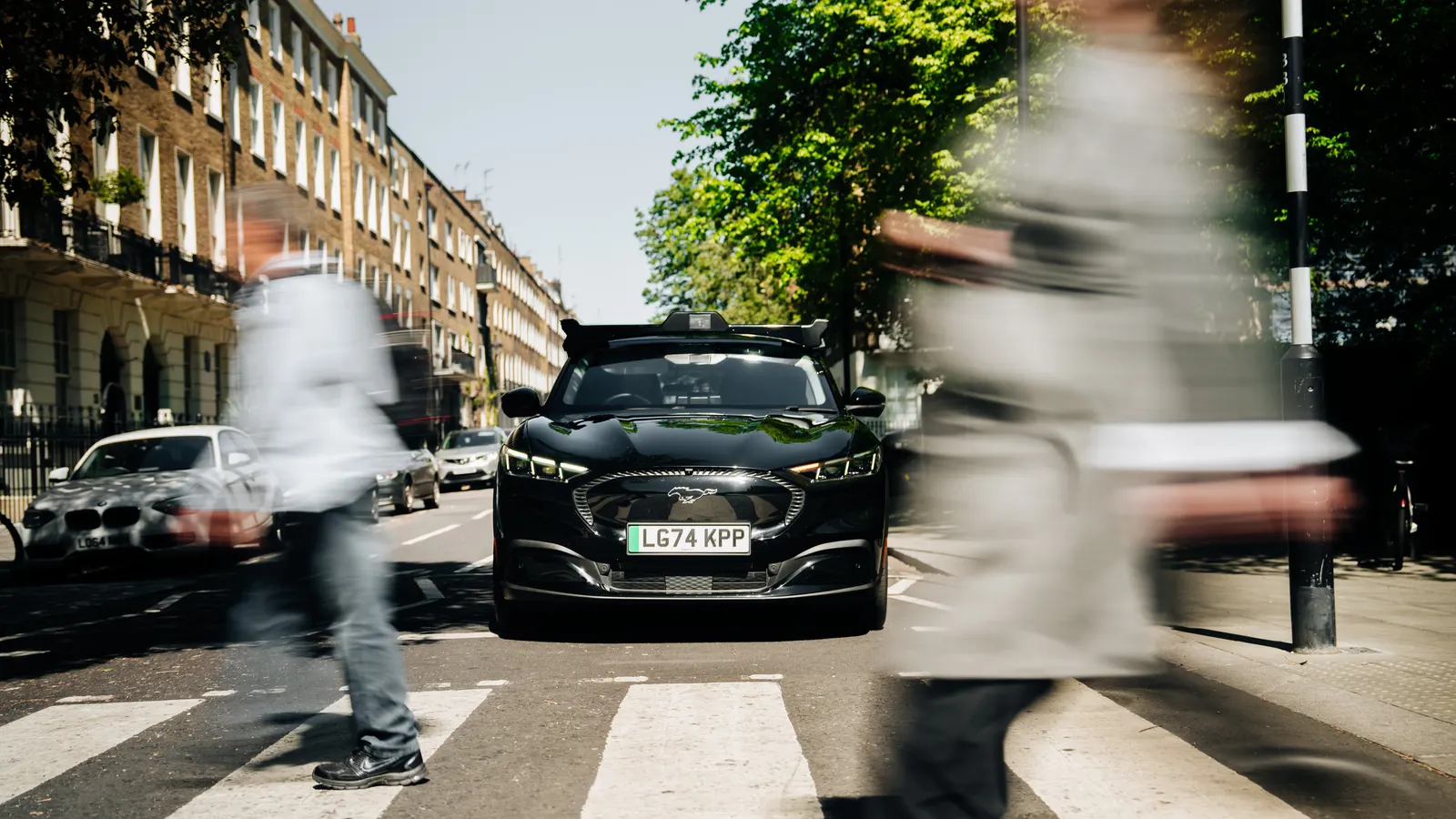 A Wayve test vehicle stopped at a zebra crossing in London, with pedestrians blurred in motion