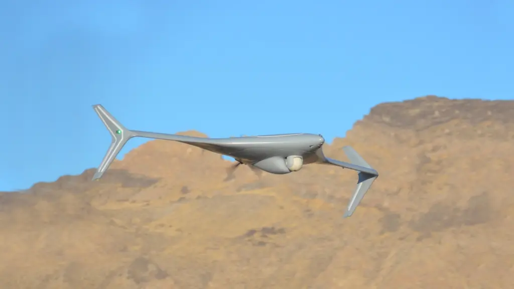 A military UAV in flight over desert terrain, with a sensor turret visible under the fuselage.